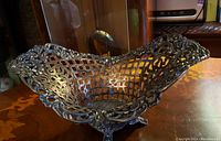 Antique silver basket viewed angled from above, showing detailed scalloped edges, lattice openwork, and reflective surface.