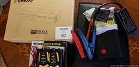Photo showing the boxed Gooloo Elite 1200A jump starter, the jump starter unit with clamps and black carrying bag alongside two keyless entry remote fobs in packaging.