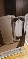 Swash dry cleaning machine in box showing transparent door with white shirt inside.
