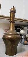 Front view of antique hand made Persian brass vessel showing overall shape and dome top with finial