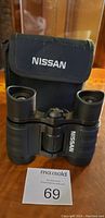 Front view of Nissan binoculars with carrying pouch, showing the front lenses and Nissan logo.