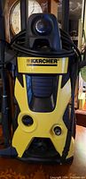 Front view of Karcher pressure washer showing yellow and black casing, power cord wrapped on top handle, and logo.