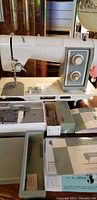 Front view of sewing machine with open accessory tray and manuals in foreground