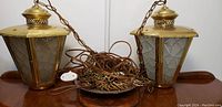 Pair of antique golden hanging lantern lights with attached long gold chains displayed on a wooden surface, showing front view.