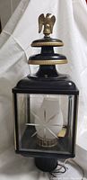 Full view of black metal antique lantern lamp with brass eagle finial, tiered top, etched glass panels, and frosted glass bulb cover inside.