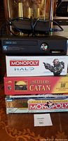 Xbox 360 console with power adaptor and three stacked unopened board games on table.