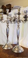 Pair of tall antique silver plated candelabra with five candle holders seen from a front angle, displaying height and design details.