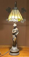 Front view of the full lamp illuminated showing stained glass shade and bronze figural base.