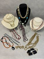 Display of assorted vintage costume jewelry including beaded necklaces, pearl necklaces, bracelet, and earrings on stands and flat