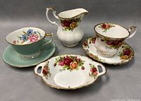 Four-piece set with two teacups and saucers, creamer, and candy bowl, showing floral china with gold trim.