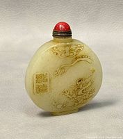 Front view of the jade snuff bottle showing embossed dragon and cloud designs with red rounded cap.
