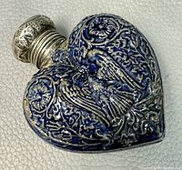 Close-up of the heart-shaped perfume bottle showing detailed silver plate repousse work, blue enamel, and bird motif.
