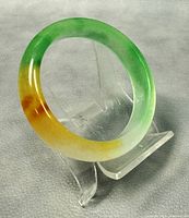 Front diagonal view of the jade bangle showing its green and yellow colors and polished finish on stand.