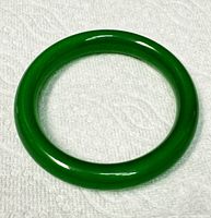 Top down photo of the smooth, polished green jade bangle on a white textured background.