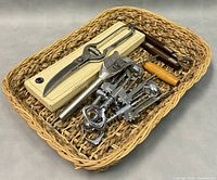 Overview of kitchen utensils in basket including Kuhn Rikon corn zipper in box, metal poultry bone shears, bottle openers, and corkscrews.