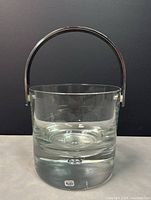 Front view of clear glass ice bucket with metal handle and original Kosta Boda label on base.