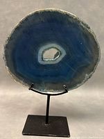 Front view of blue-green polished geode slice on black metal stand showing crystal cavity center and layered bands.