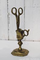 Brass candle snuffer with matching holder exhibited together, showing details of handle and base.