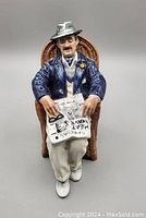 Front view of Royal Doulton "Taking Things Easy" HN2677 figurine showing seated man reading newspaper with glasses, wearing blue jacket and grey hat.
