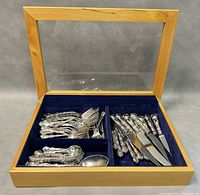 Full lot overview showing wooden lift-top display case open with blue velvet compartments holding flatware pieces