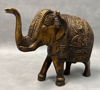 Front-left angled view of the bronze elephant sculpture showing detailed engraved designs on head and back.