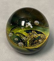 Close-up image showing the glass paperweight with green and yellow internal design and air bubbles, minor scratches visible on surface.