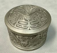 Front angle showing the pewter box body and lid featuring traditional Haida bear spirit engravings.