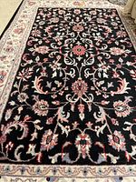 Full view of one area rug showing black floral pattern with cream border on hardwood floor.