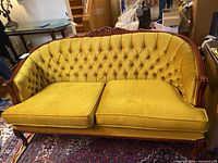 Front view of mustard yellow tufted loveseat with two seat cushions and carved wooden frame