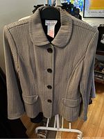 Marisa Minicucci women's light herringbone jacket with rounded collar and button closure shown on hanger.