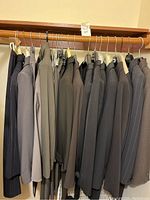 Full overview of suits hanging on wooden rod, various colors and styles