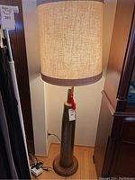 Full view of the artillery shell base floor lamp showing its height and large beige drum lampshade.