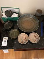Overview of assorted clay bowls and coasters on black surface including large bowl, smaller bowls, and coasters in box