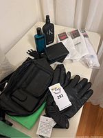 Multiple black leather gloves, black leather wallets, black leather fanny pack, two bottles of Calvin Klein cologne, and white sports socks arranged on a table.