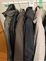 Five jackets hanging on rack: grey, black leather, brown, black, beige.