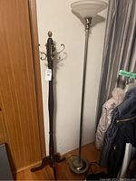 Photo showing both the wooden coat tree and metal floor lamp side by side against a wall with a curtain on the right and a wooden door on the left.