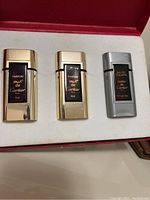 Three miniature Cartier cologne bottles in a red presentation box, two gold and one silver, each labeled with 'Parfum Must de Cartier' or 'Eau de Toilette Must de Cartier'