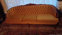 Full view of gold tufted back sofa with carved wood trim and three seat cushions