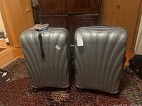Front view of two silver Samsonite suitcases side by side on a patterned rug.