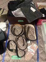 Photo showing several scarves in dark colors on top of a box, with four belts and a pair of gloves laid out around it.