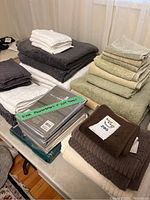 Wide view of assorted towels, face cloths, king pillowcases, and flat sheets on a table, showing stacks of folded towels and packaged bed linens.