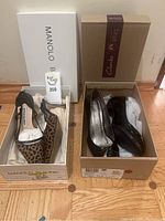 Pair of Manolo Blahnik leopard print slingback high heels and Clarks black leather flats in their respective boxes on wood floor.