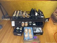 Photo showing multiple pairs of women's shoes on a black metal shoe rack with three shelves, along with shoeboxes underneath.