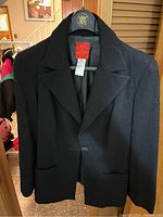 Front view of black women's blazer with textured floral pattern on fabric, hanging on a hanger.