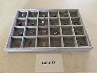 Full view of 19 jewelry pieces including rings and pendants displayed in grey velvet tray