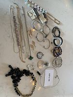 Photo showing collection of necklaces, bracelets, earrings including pearl necklace, multiple silver and gold chains, and various bracelets and earrings on a marble surface.