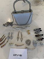 Full view of silver Farnell Paris handbag and assorted jewelry laid out: brooches, earrings, decorative hair pins.