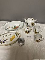 Front view of the full set on a white tablecloth: teapot, sugar bowl, two creamers, covered casserole, oval baker, egg coddler.
