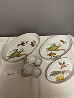 Photo showing three oval porcelain serving dishes with different fruit and vegetable illustrations and six porcelain ramekins with berry design.