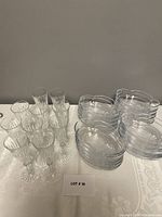 Overview photo showing all 10 clear patterned glass flutes and 20 oval dessert bowls placed neatly on a white tablecloth.